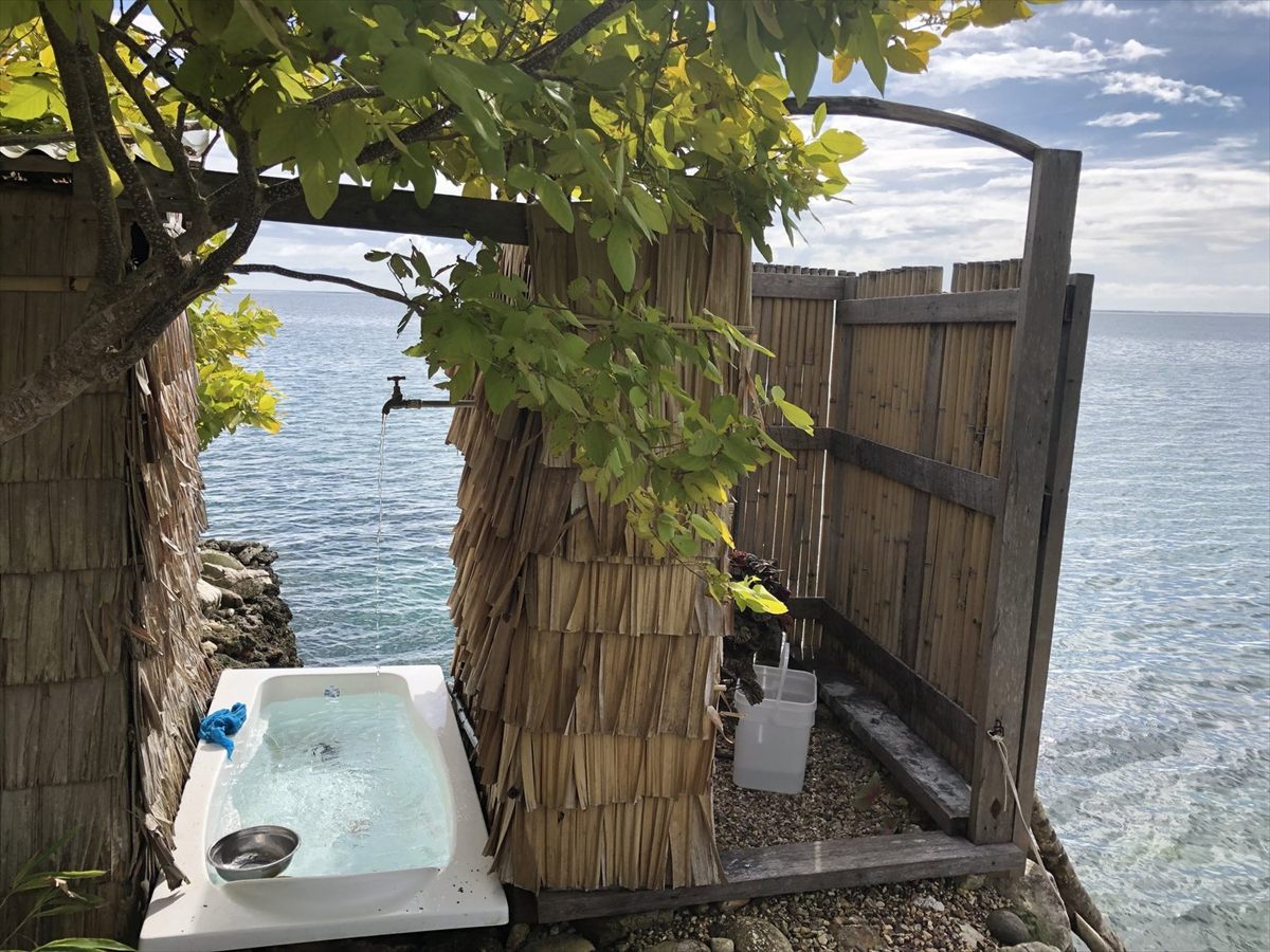 An open-air bath in a thatch and bamboo enclosure, looking straight out over the lagoon