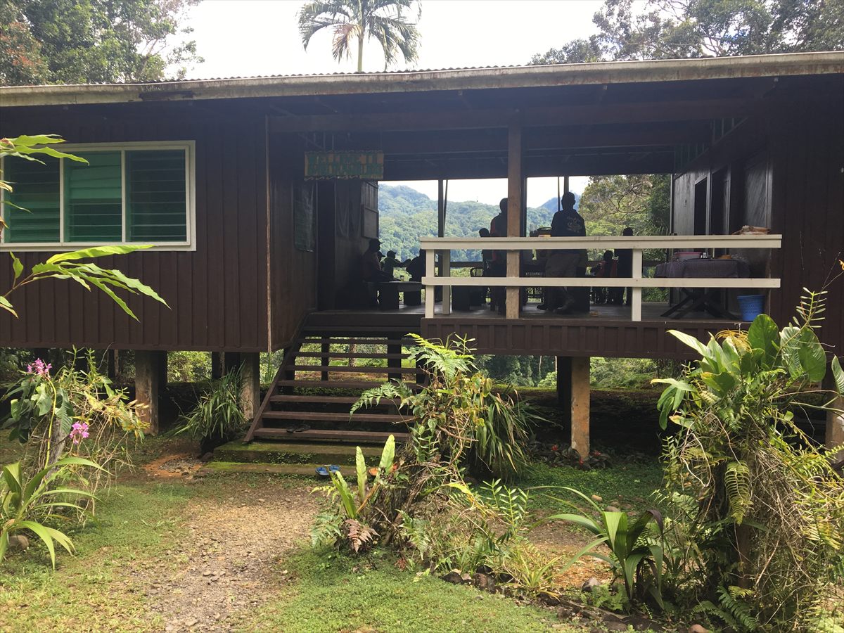Imbu Rano Lodge, a dark timber building on stilts with an open balcony looking out to forested hills