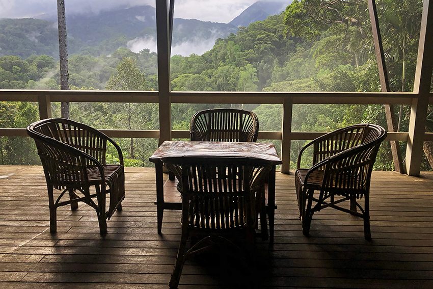 Cane chairs on the lodge balcony facing misty, rainforest-covered mountains