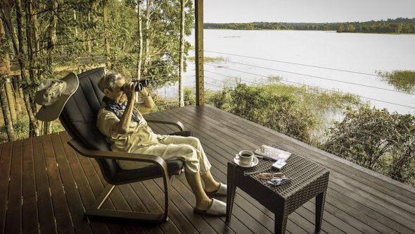 A guest birdwatching with binoculars from a timber veranda above the lake
