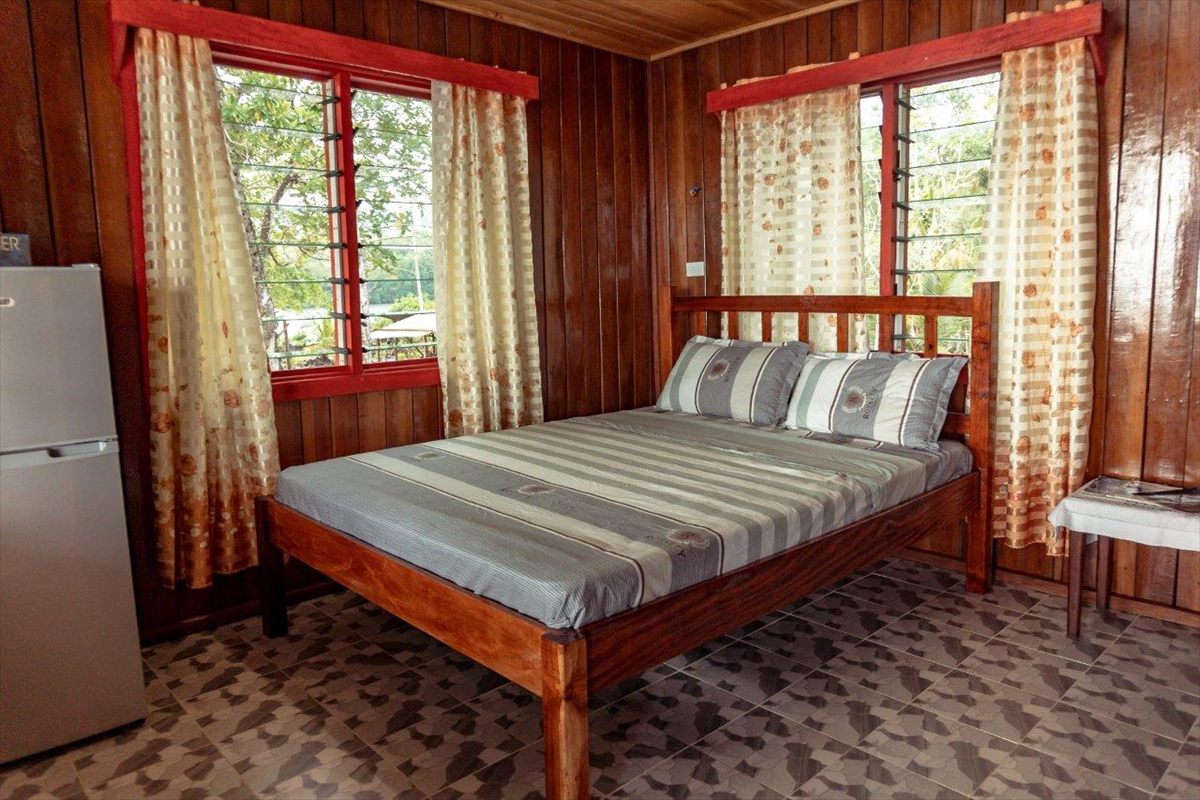 A queen-sized bed in a timber-lined bungalow room with louvred windows