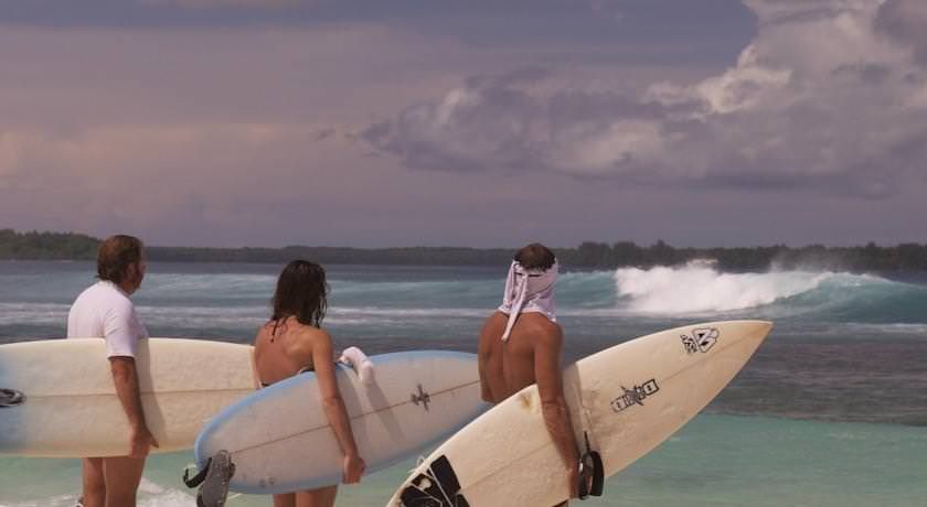 Three surfers holding their boards, watching a wave break on the reef