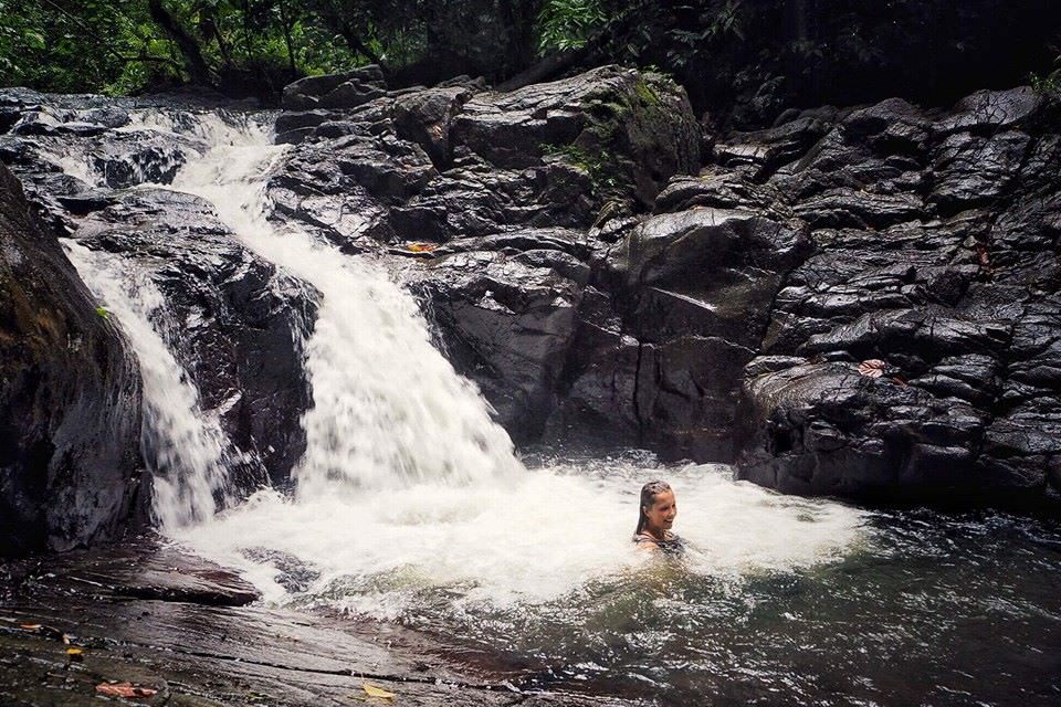 A swimmer in the pool at the foot of a rainforest waterfall