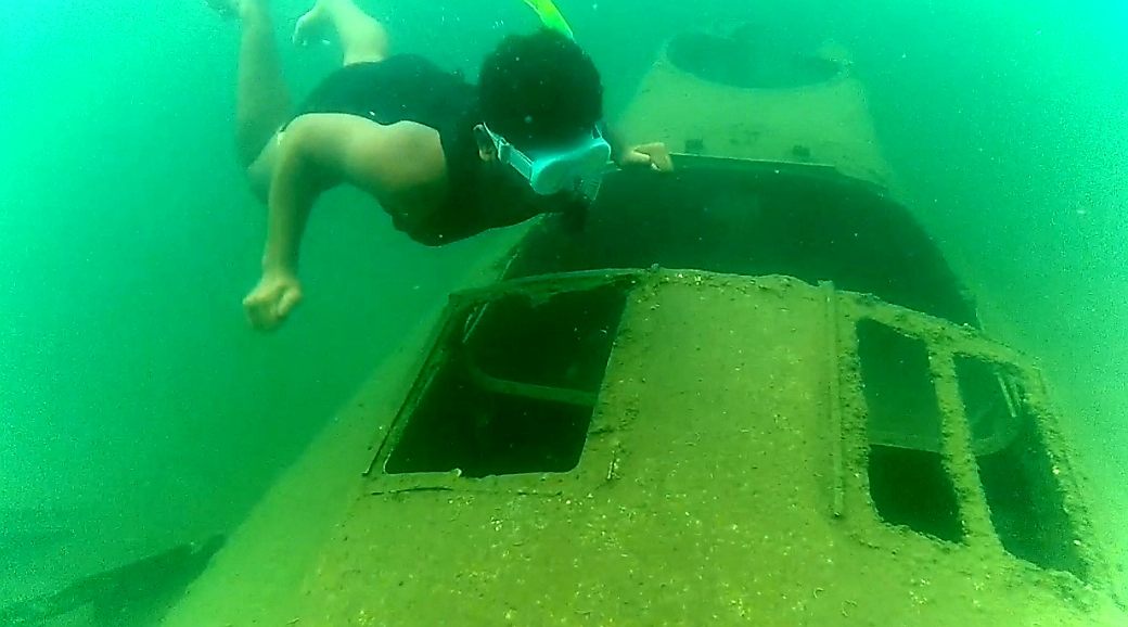 A snorkeller swimming over a sunken WWII relic in green water