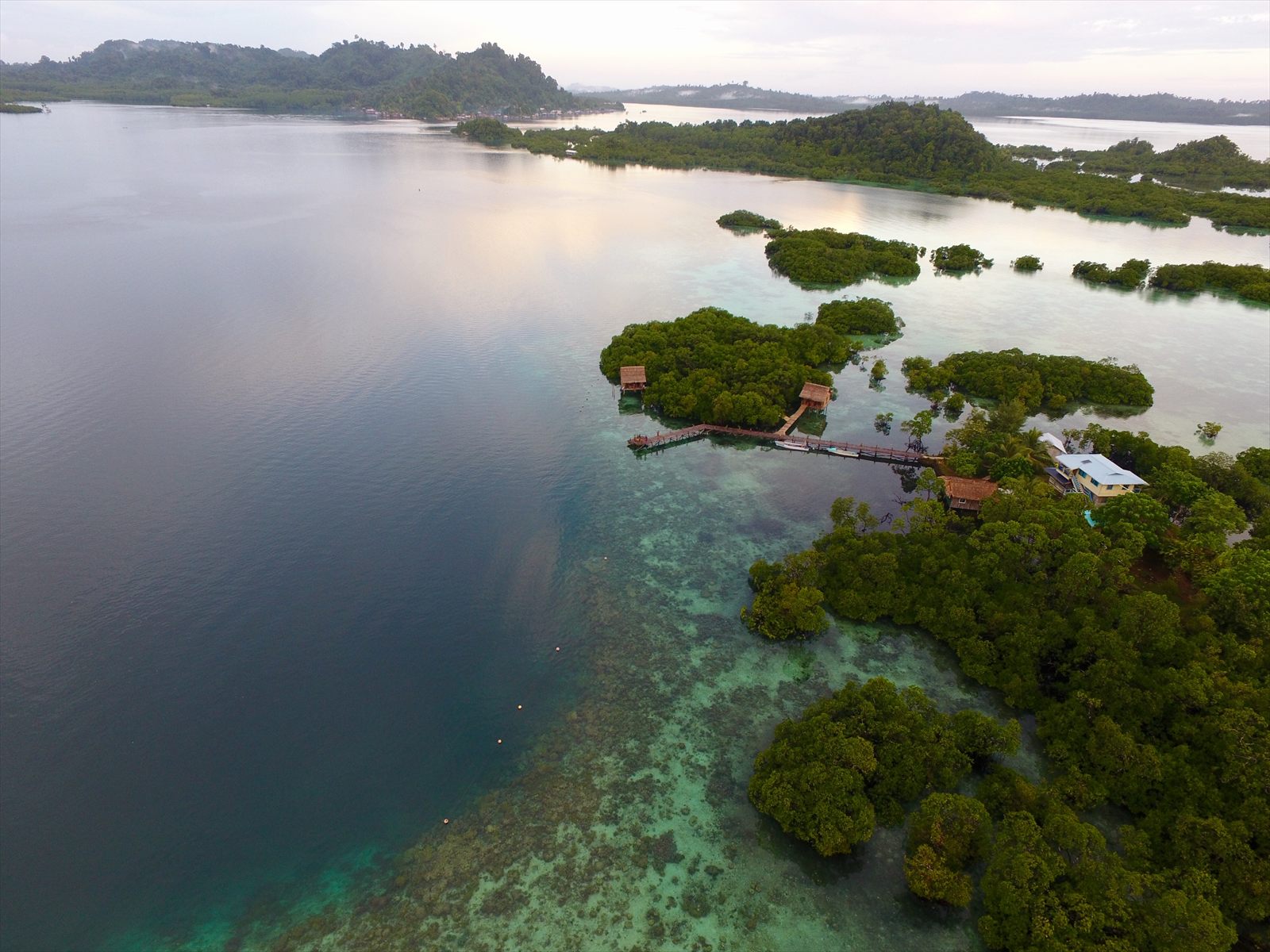 Aerial view of Noguna Island Homestay’s jetty and bungalows on stilts among mangrove islets and coral shallows