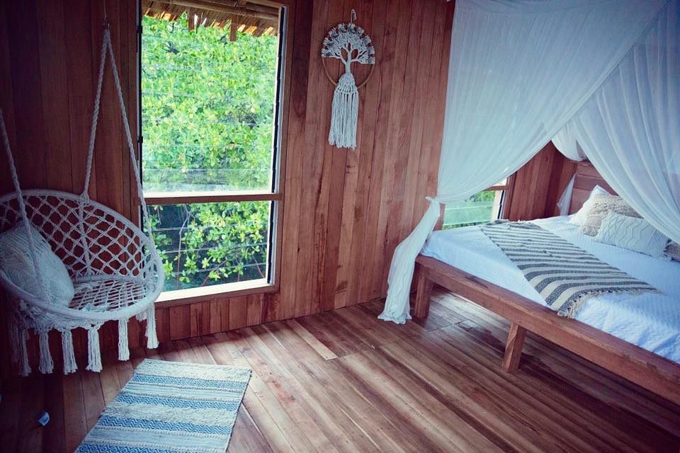A timber-lined bedroom with a mosquito-netted bed and a hanging woven chair