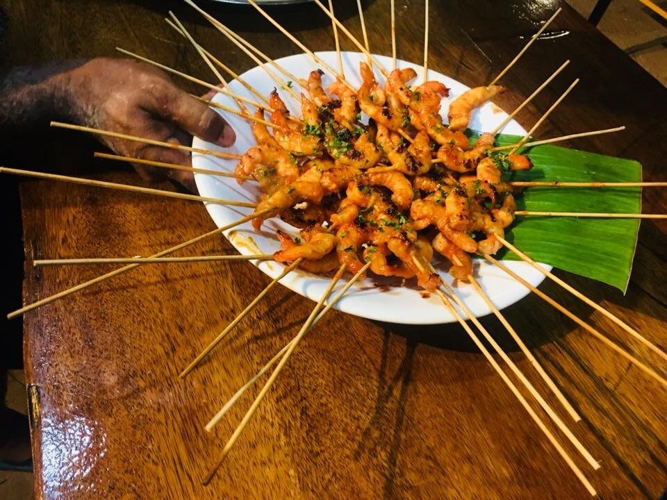 A plate of grilled prawn skewers on a banana leaf