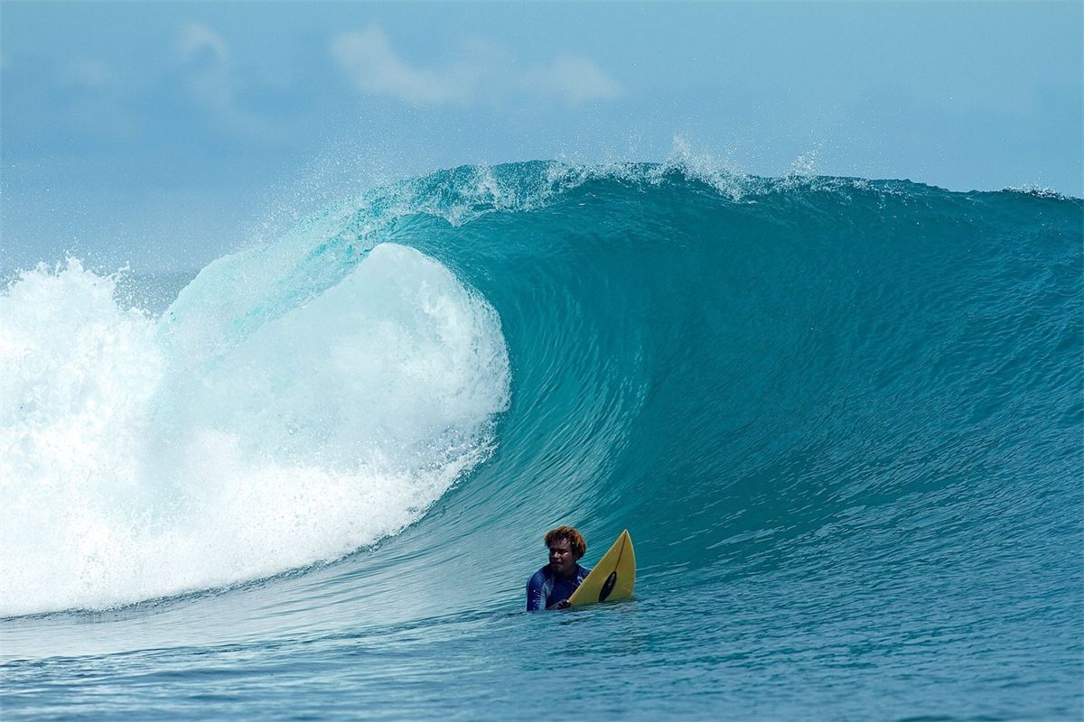 A surfer in the water beside a curling turquoise wave
