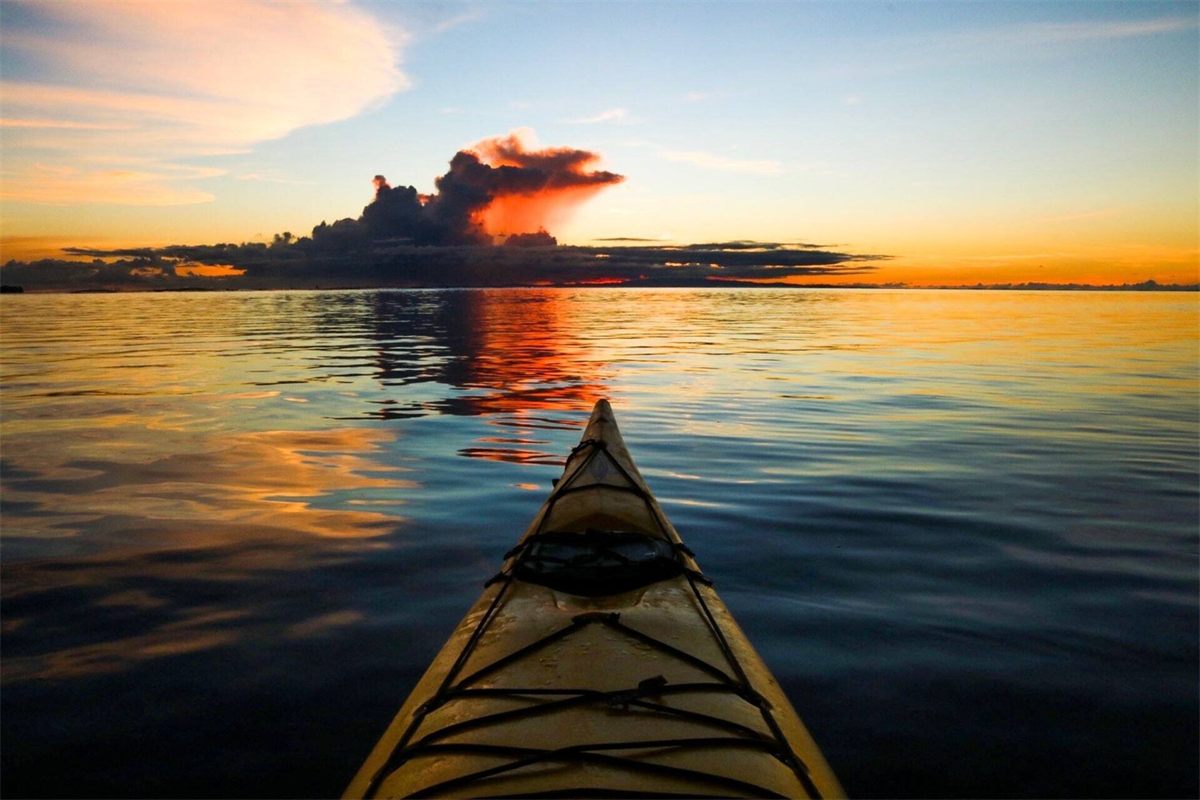 The bow of a kayak on calm water at sunset