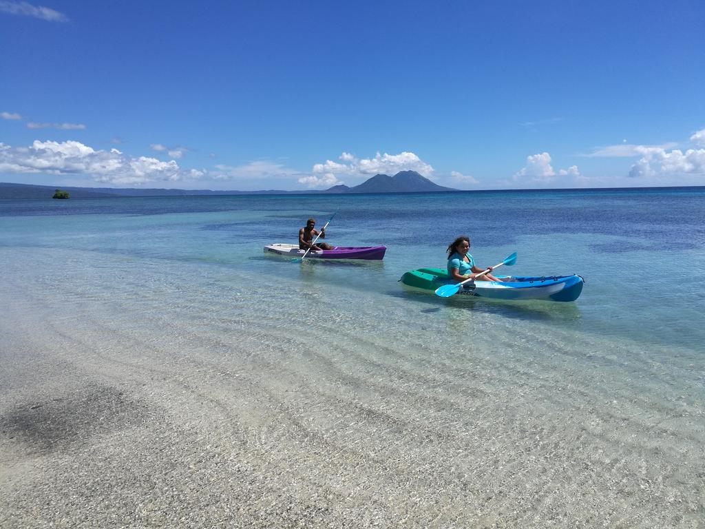 Two kayakers paddling over clear shallows off Rapopo, with volcanic peaks on the horizon