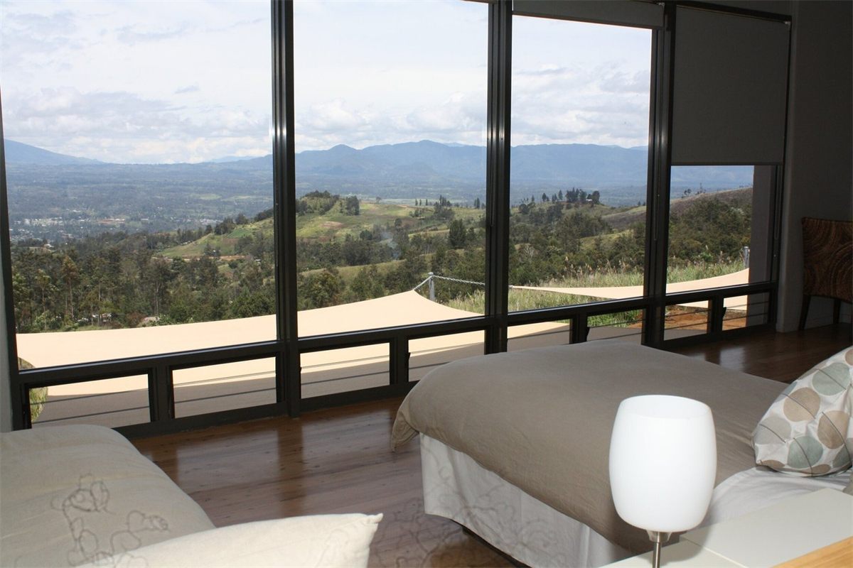 A guest room at Rondon Ridge with floor-to-ceiling windows looking out over green hills and the valley below