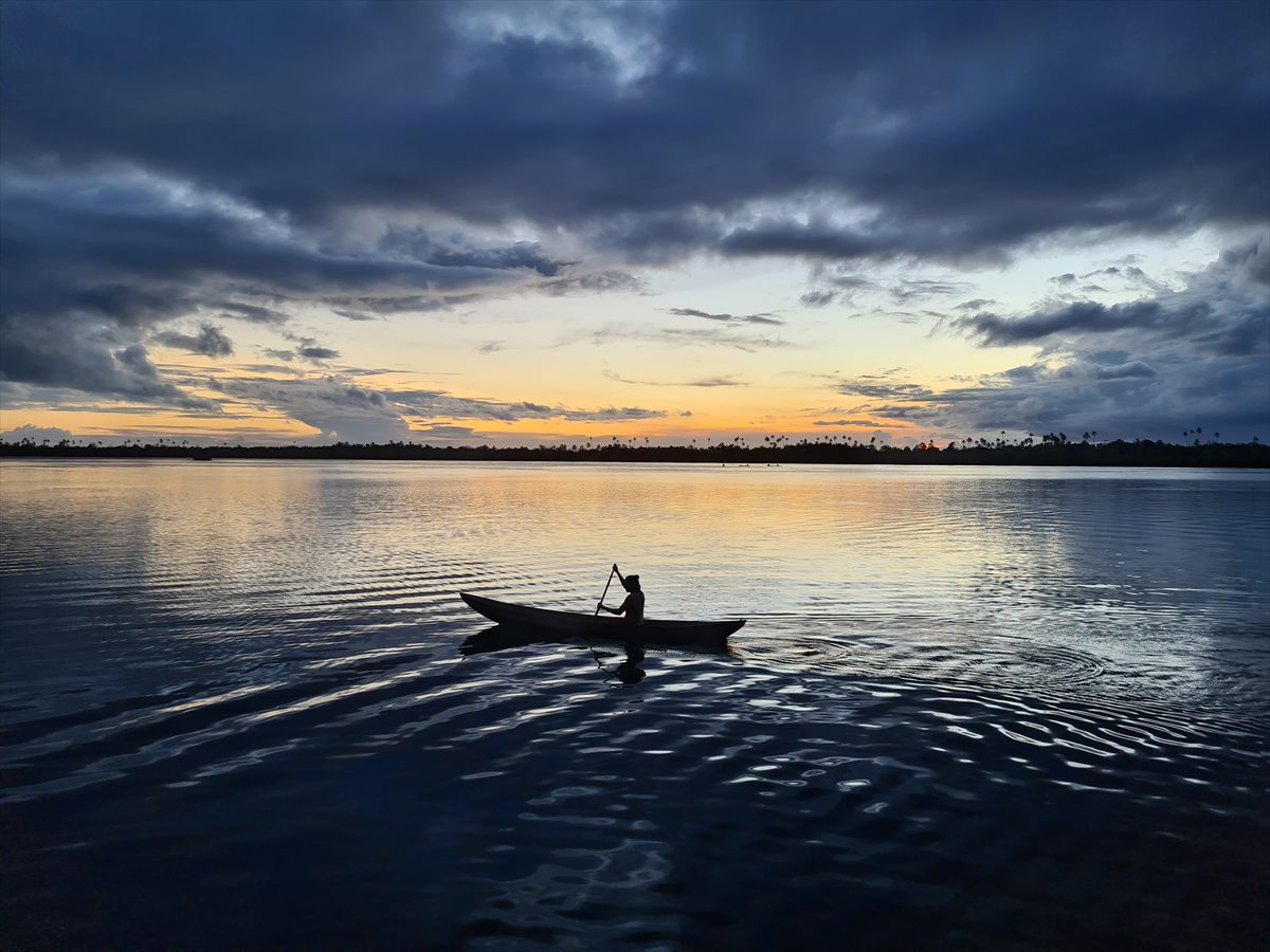 A lone paddler in a dugout canoe silhouetted against a Langa Langa Lagoon sunset