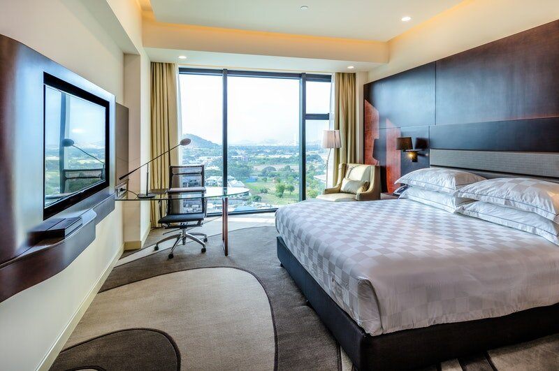 A deluxe room at The Stanley with a large bed, a work desk and city views