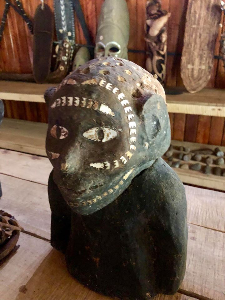 A traditional carved figure inlaid with shell, with more carvings displayed on shelves behind