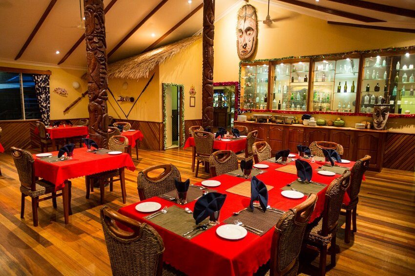 Tables set with red cloths in Tawali’s restaurant, with carved posts and a timber floor