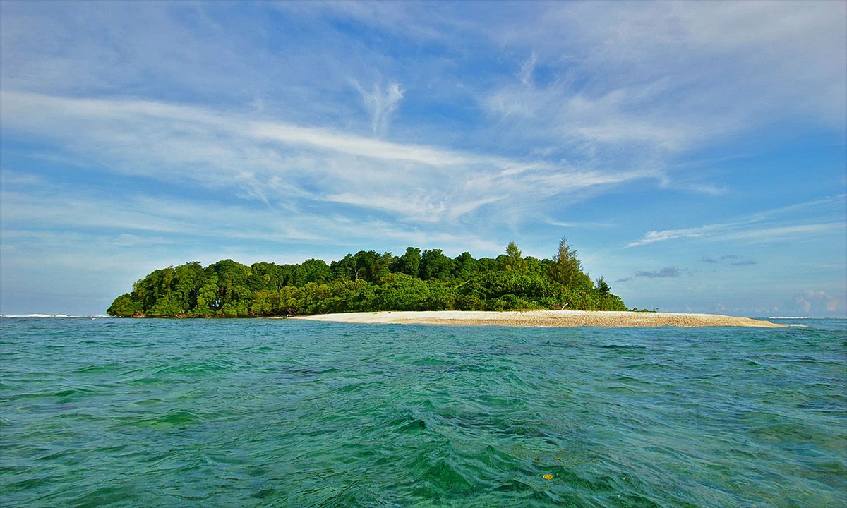 A forested island with a long white sand spit across turquoise water