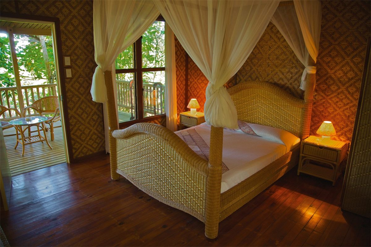 A four-poster bed inside a timber-floored bungalow at Tufi Resort, with doors open to the verandah