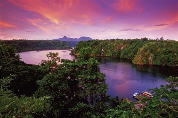 Sunset over the rainforest-lined fjord below Tufi Resort, with mountains on the horizon