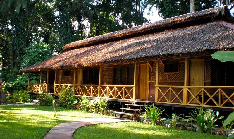A thatched block of guest rooms with a shared verandah, set on lawns at Walindi