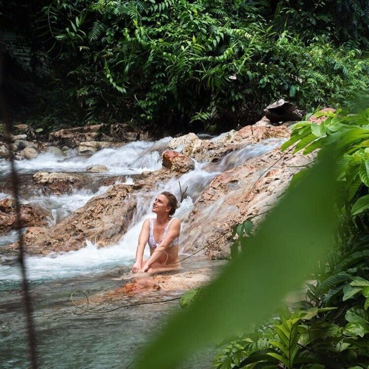 A swimmer sitting in a warm rainforest river cascade